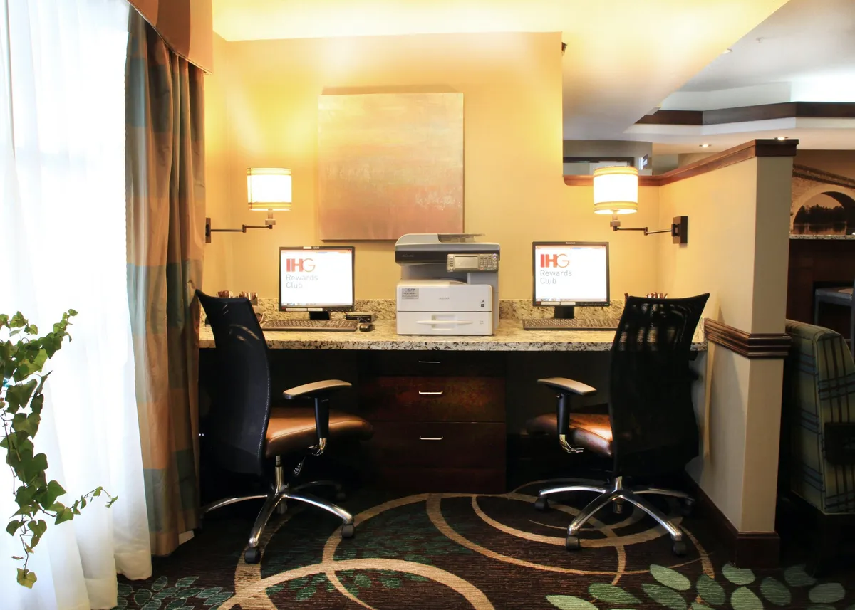 A practical workspace featuring computer stations on a granite countertop, contemporary lighting, and stylish wall art. The area is calm and conducive to productivity, supporting business or study needs.