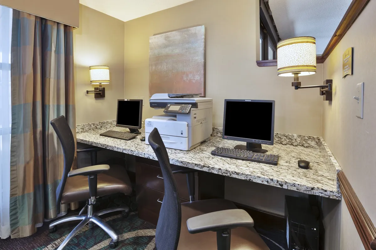A bright, functional business center featuring computers, a printer, and a sleek granite counter—designed for productivity and convenience. The space is inviting for guests needing to work or catch up on business tasks.