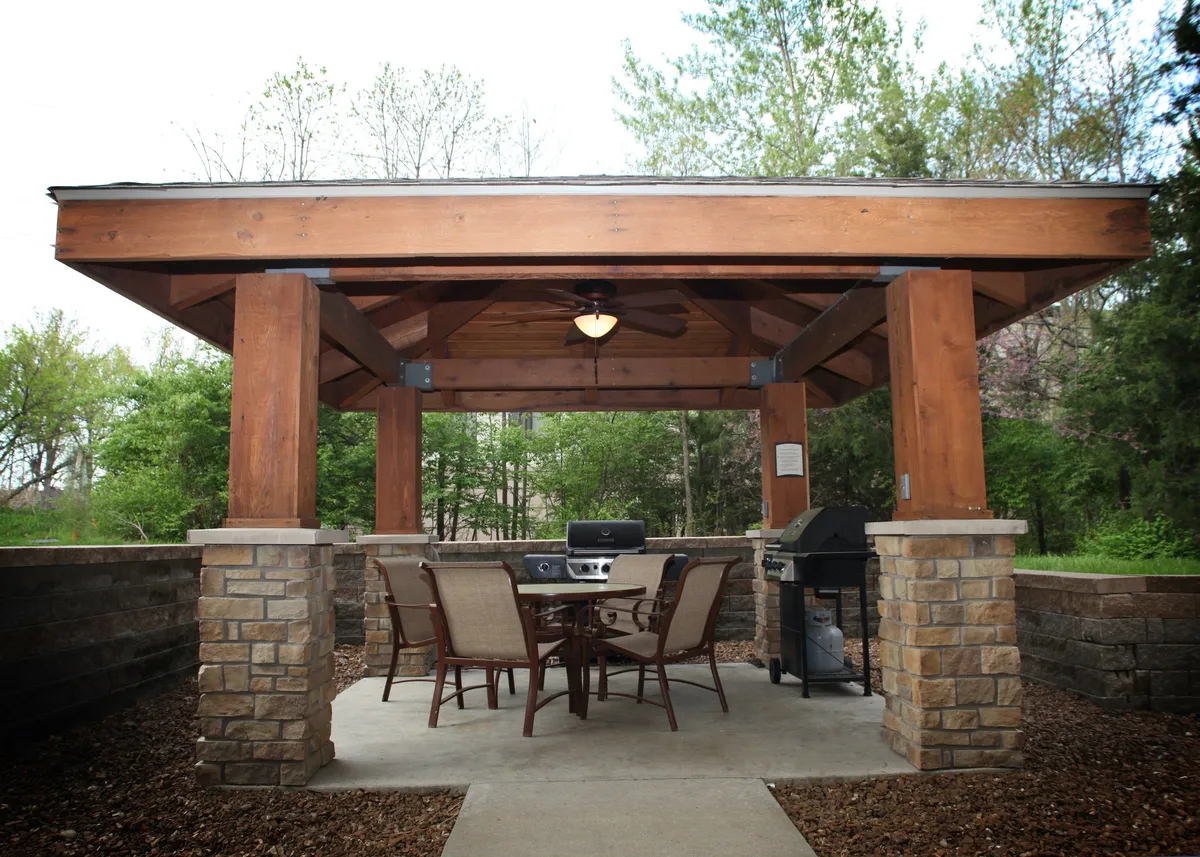 This image showcases a charming wooden pavilion set outdoors, featuring a dining table and grill. The setting evokes the feeling of summer barbecues and relaxed outdoor meals, with ample space for couples to enjoy a quiet evening or celebrate a special occasion together. The surrounding greenery adds to the serene, inviting atmosphere that encourages leisure and connection.
