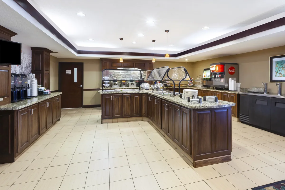 This image displays a buffet counter with a coffee station, beverage dispenser, and food display, reflecting the complimentary breakfast buffet and social aspect of meal times. The space is casual and welcoming, making it ideal for morning rituals and community events.