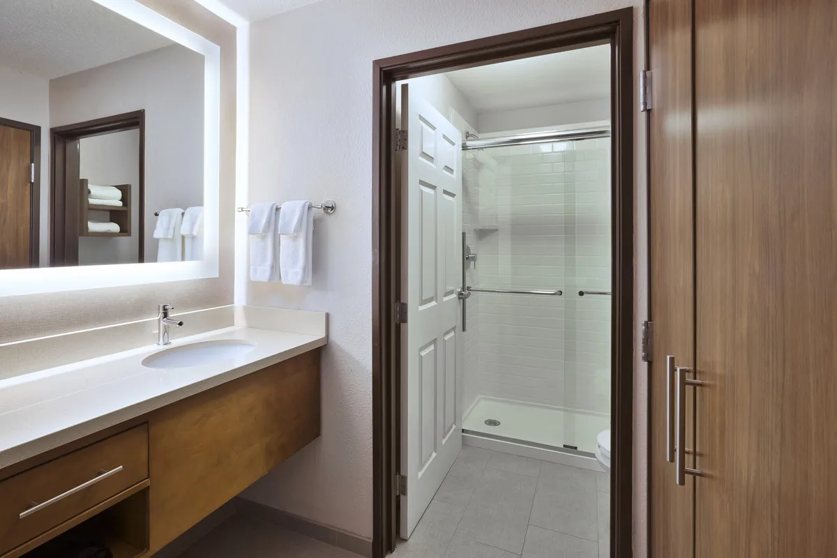 A modern ensuite bathroom with a sleek vanity mirror, spacious shower area, and warm wooden cabinetry. The bathroom is spotless and inviting, with fluffy towels and bath amenities visible, emphasizing a spa-like atmosphere ideal for self-care and relaxation.