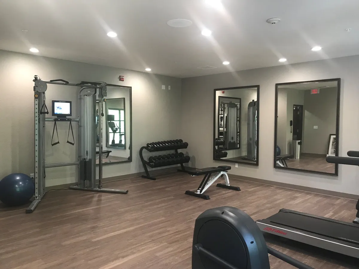 A dynamic gym space outfitted with multifunctional gym equipment, a dumbbell rack, exercise ball, and full-length mirrors. Guests can be seen working out, engaging in personal training sessions, or joining group fitness classes.