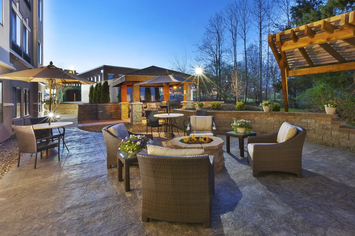 An inviting exterior seating area with a fire pit, outdoor chairs, umbrellas, and a pergola. The setting encourages evening relaxation, storytelling, and socializing after a day of activities.