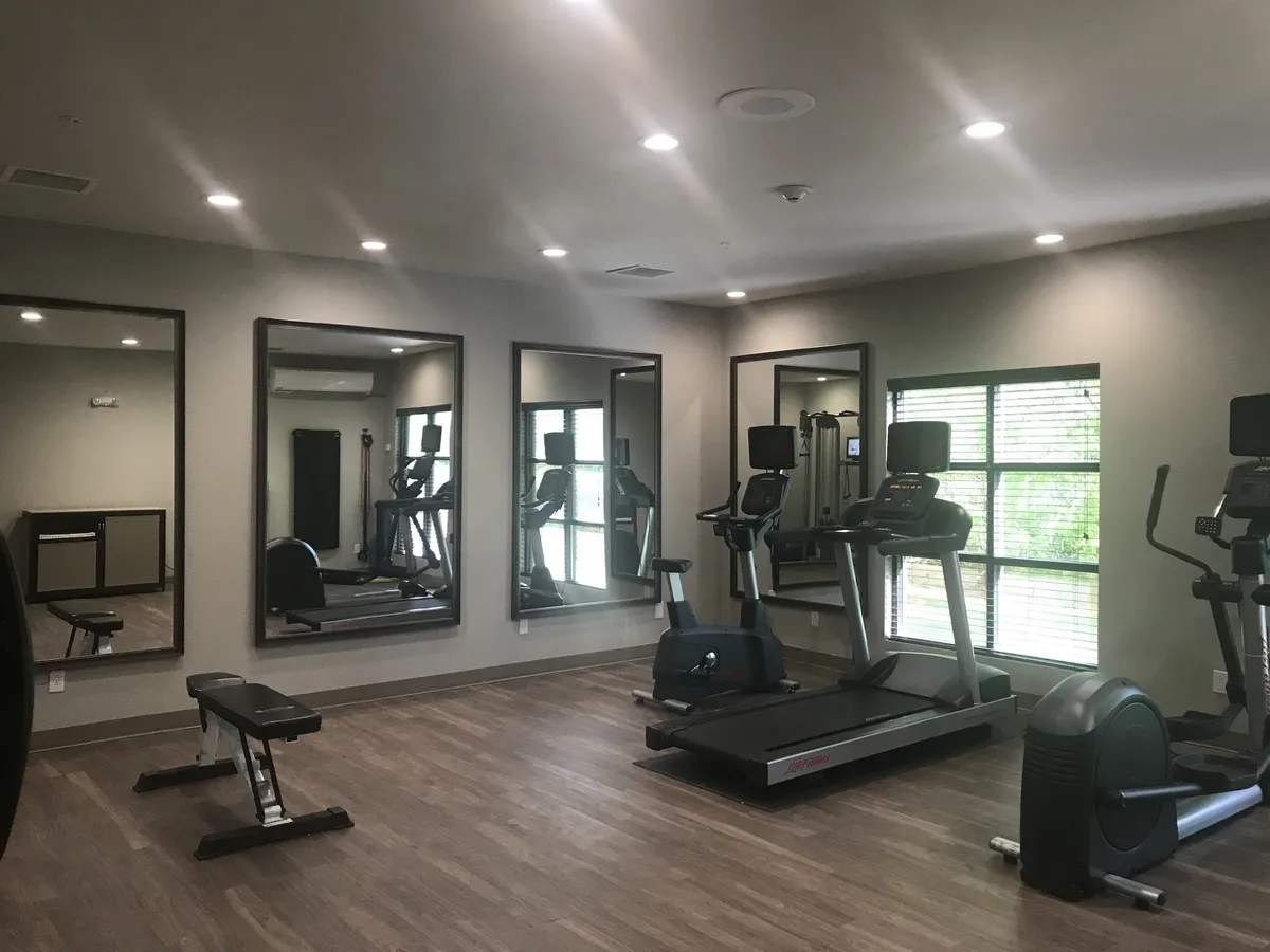 An interior view of the on-site fitness center, equipped with treadmills, elliptical machines, mirrors, and an exercise bench. The space is bright, clean, and designed for focused workouts, aligning with both productivity and wellness.