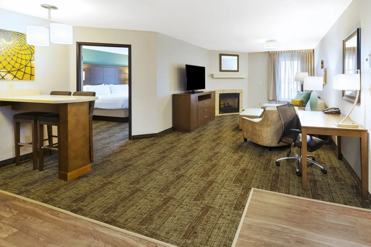 A cozy, sunlit living area featuring bar seating, a television, a fireplace, and a laptop-friendly workspace with an armchair. The room is individually decorated and offers both comfortable seating for relaxation and a dedicated spot for remote work.