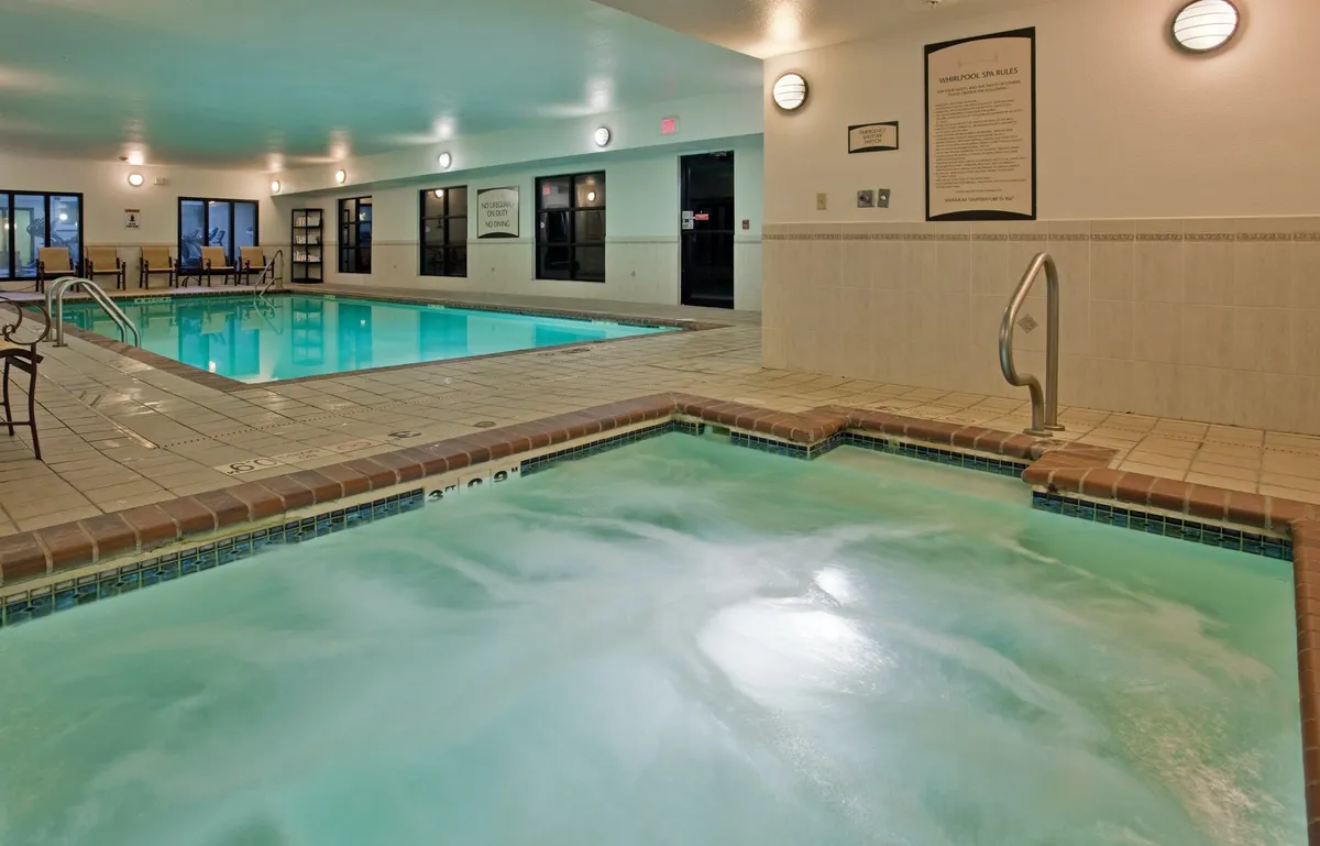 This image captures a serene indoor pool area featuring both a sparkling swimming pool and a bubbling hot tub, surrounded by lounge chairs. The atmosphere is calm and rejuvenating, suggesting a perfect spot to unwind after a busy day or socialize with fellow guests.