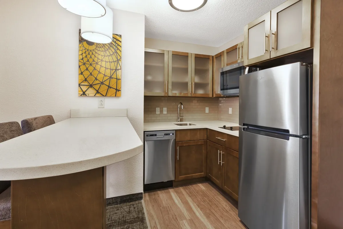 This image features a modern, cozy kitchen with a bar counter and stainless steel appliances. The layout suggests a well-equipped, inviting environment ideal for cooking and socializing. Artwork on the wall adds a homey touch, and the visible appliances underline the practicality for guests who enjoy preparing meals.